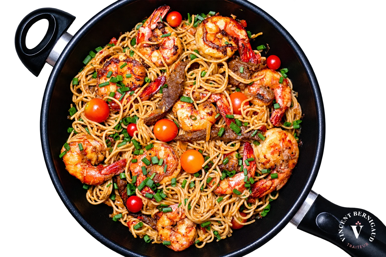 Vue de dessus d'une grande poêle noire remplie de spaghettis sautés avec des crevettes, des lanières de bœuf, des tomates cerises et de la ciboulette.